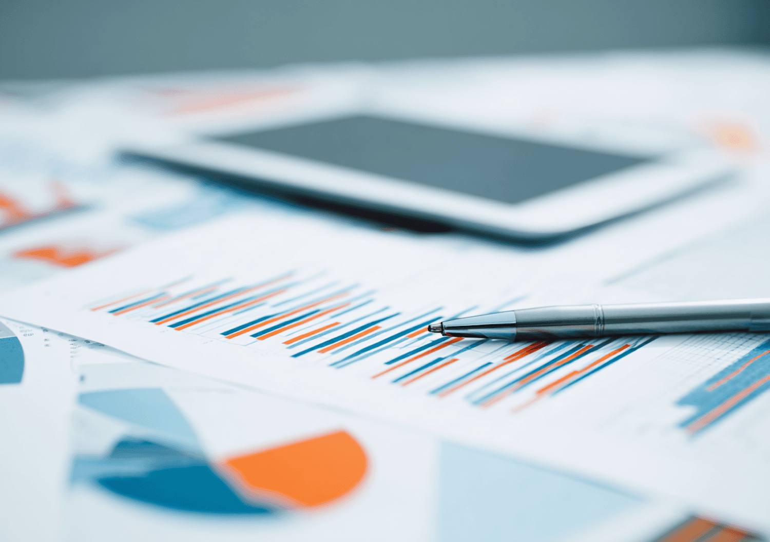 Printed revenue charts and a silver pen next to a tablet on a desk